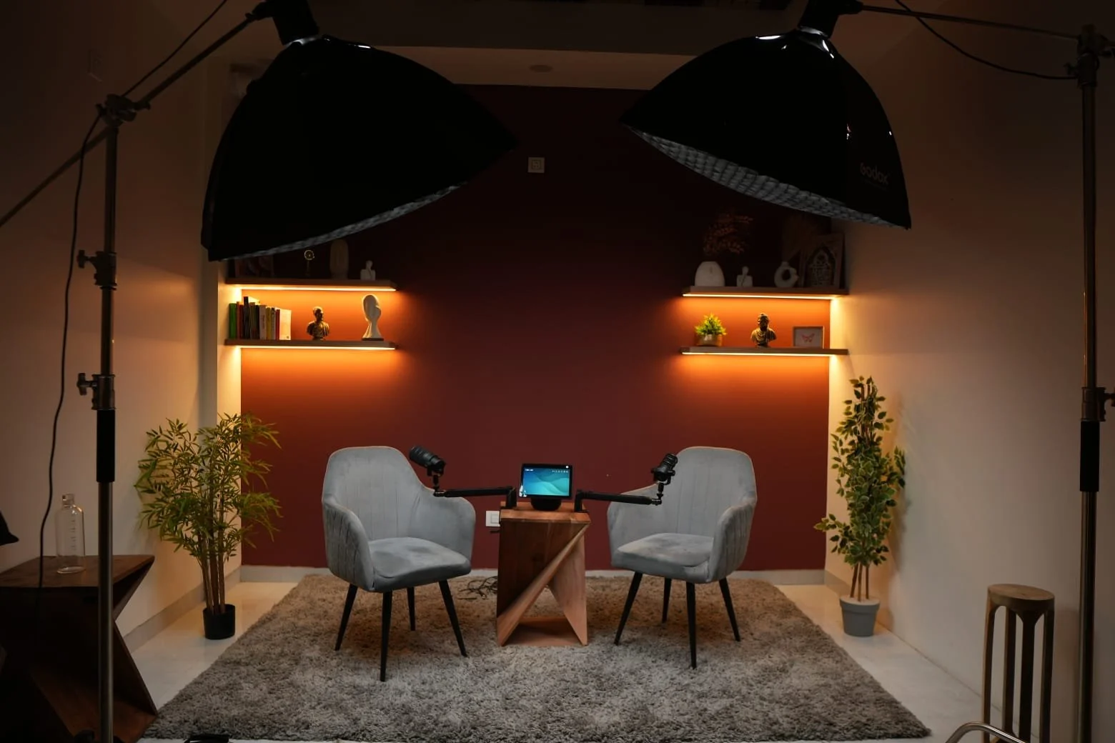 A two-seat podcast set with microphones on boom arms and two overhead softbox lights