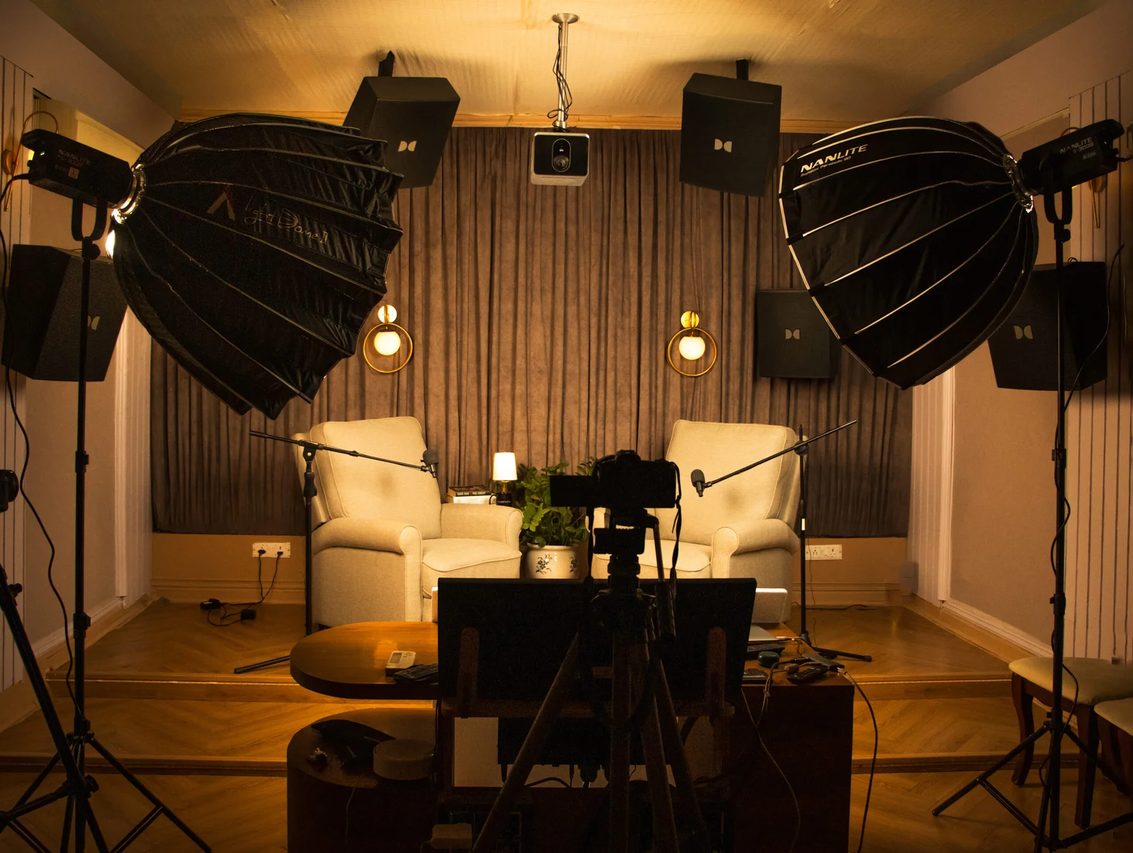 A studio set with two armchairs lit by large softboxes, with a camera on a tripod in the foreground